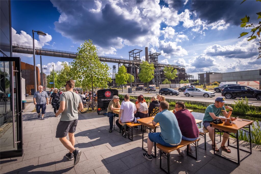 Menschen aus Dortmund sitzen bei gutem Wetter draußen vor der Bergmann Stehbierhalle Phönix-West.
