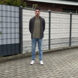 Mert Erdem steht auf einer leeren Fläche zwischen zwei belegten Parkplätzen am Fahrbahnrand.