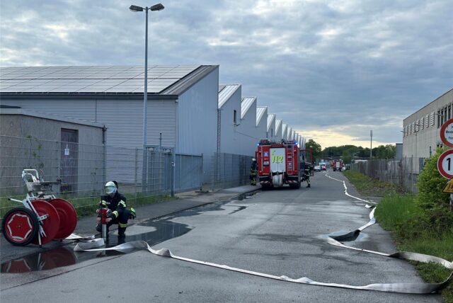 Blick auf die Zufahrt der Maschinenhallen, in der einige Löschfahrzeuge stehen und ein Löschschlauch ausgerollt ist