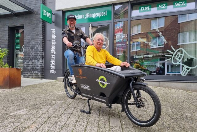 Zwei Männer sitzen in einem Lastenfahrrad.