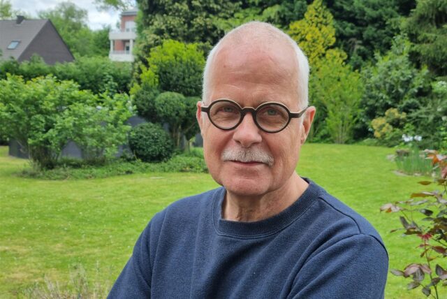 Ein Mann mit Brille steht in seinem Garten.