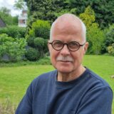 Ein Mann mit Brille steht in seinem Garten.