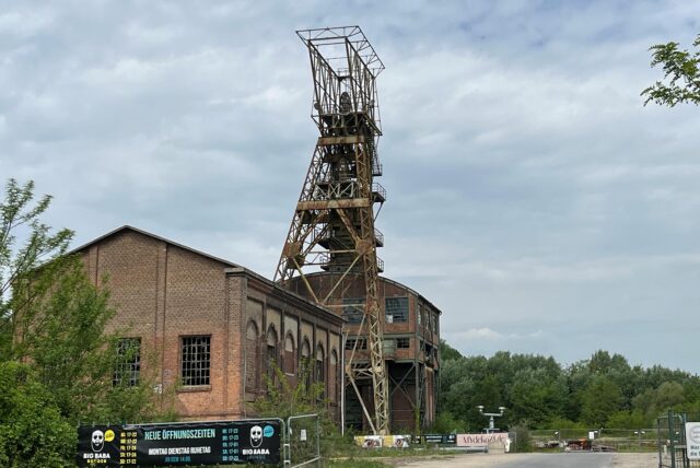 Das Foto zeigt ein altes Industriegebäude mit einem Förderturm davor.