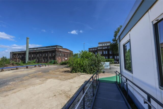 Die Fassade des historische Stahlbungalows ist zu sehen, im Hintergrund erkennt man das Gelände der Westfalenhütte.