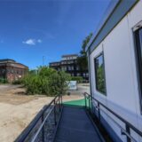 Die Fassade des historische Stahlbungalows ist zu sehen, im Hintergrund erkennt man das Gelände der Westfalenhütte.