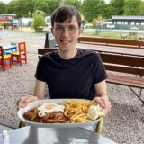 WZ-Autor Valentin Schneider hält einen Teller mit Schnitzel und Pommes im Außenbereich der Gaststätte Königsmoor in Waltrop.