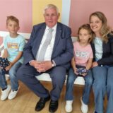 Minister Laumann sitzt mit zwei Kindern und einer Frau auf einer weißen Bank.