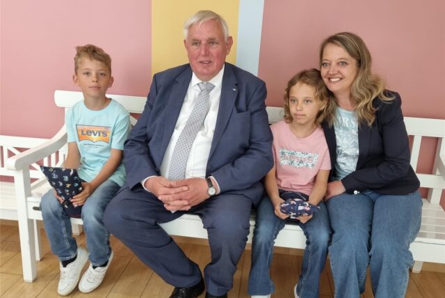 Minister Laumann sitzt mit zwei Kindern und einer Frau auf einer weißen Bank.