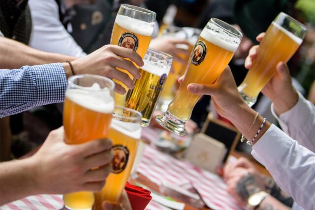 Menschen stoßen mit Weizengläsern in einem Biergarten an.