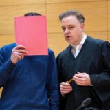 Anwalt Burkhard Benecken mit einem Angeklagten, der sich einen Ordner vor das Gesicht hält.