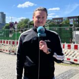 Tim Hübbertz steht mit einem Mikrofon in der Hand in der Dortmunder Nordstadt und berichtet über eine Großbaustelle.