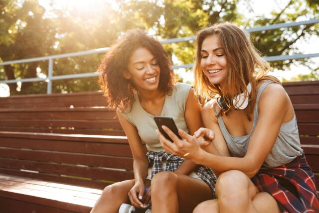 Zwei Frauen sitzen nebeneinander und gucken auf ein Handy.