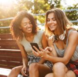 Zwei Frauen sitzen nebeneinander und gucken auf ein Handy.
