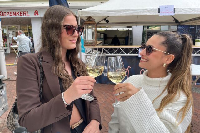 Zwei Frauen stoßen mit einem Glas Wein an.