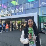 Die Front des Hauptbahnhofs Recklinghausen. Davor steht Reporterin Rosi Taslima Azam mit einem Mikrofon in der Hand.