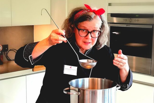 Elke Schumacher steht mit einem großen Schöpflöffel an einem Suppentopf.
