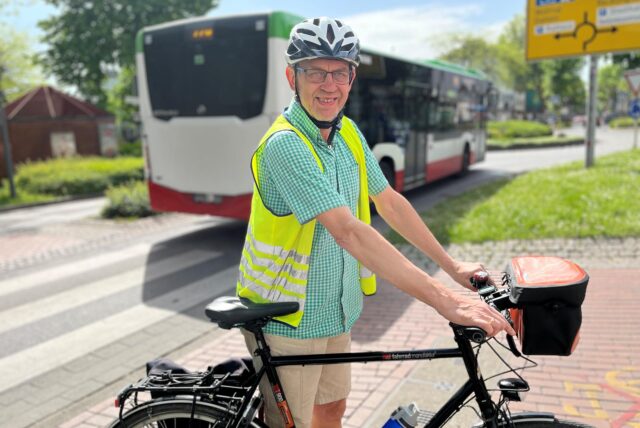 Ein Mann mit Warnweste und Fahrradhelm lächelt in die Kamera.