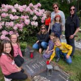 Neun Schüler der OGS-Hullern stehen gemeinsam mit OGS-Leiterin Meike Rabenschlag und pädagogischen Fachkraft Marie Backhaus an einem Grab. Sam legt eine Gedenkkerze nieder.