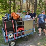 Ein Maiwagen mit einer Gruppe Menschen dahinter. Der Maiwagen hat Musikboxen mit an Board.