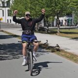 Ein junger Mann fährt auf dem Fahrrad, seine Freunde feuern ihn an.