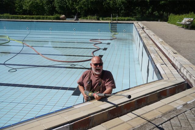 Jürgen Kaldeweide steht in einem leeren Schwimmbecken, mit einer Hochdruckmaschine in der Hand.