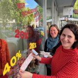 Zwei Frauen bekleben das Schaufenster eines Geschäfts mit Hinweisen auf Sonderangebote.