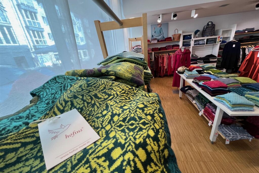 In einem Geschäft liegt farbenfrohe Damenoberbekleidung auf Tischen und Regalen oder hängt auf Bügeln. In einem Geschäft liegt farbenfrohe Damenoberbekleidung auf Tischen und Regalen oder hängt auf Bügeln.