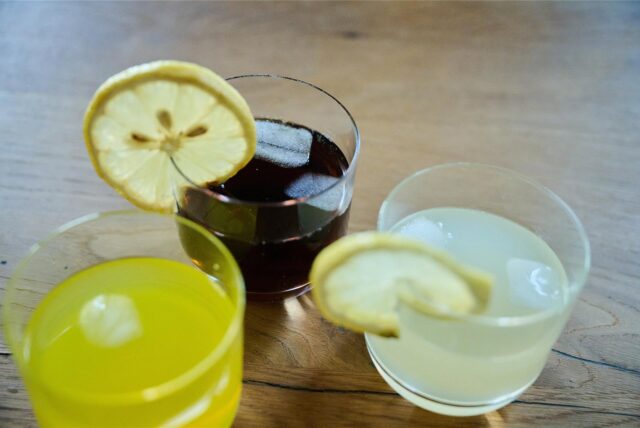 Drei Gläser Limonade, teilweise mit Zitronenscheibe, stehen auf einem Tisch.