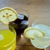 Drei Gläser Limonade, teilweise mit Zitronenscheibe, stehen auf einem Tisch.
