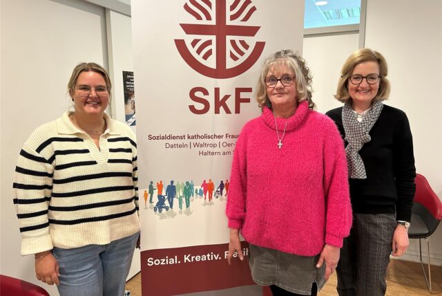 Drei Frauen stehen vor einem Banner mit der Aufschrift „SkF – Sozialdienst katholischer Frauen“.
