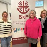 Drei Frauen stehen vor einem Banner mit der Aufschrift „SkF – Sozialdienst katholischer Frauen“.