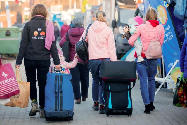 Menschen auf der Flucht, die Kinder auf dem Arm tragen oder an der Hand halten und Koffer hinter sich herziehen.