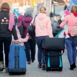 Menschen auf der Flucht, die Kinder auf dem Arm tragen oder an der Hand halten und Koffer hinter sich herziehen.
