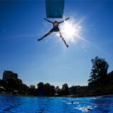 Ein Junge springt bei Sonnenschein und von einem Sprungturm in das Schwimmbecken eines Freibades.