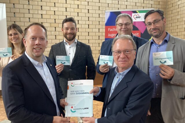 AWO-Quartiersmeister Stefan Schmitz (vorne r.) empfängt den Förderbescheid über 413.000 Euro aus den Händen von Marco Schmitz (vorne l.) Viel Erfolg wünschen dem Projekt (v. l.) die leitenden AWO-Mitarbeiter Ann-Katrin Purck, Felix Groß, AWO-Geschäftsführer Westliches Westfalen Uwe Hildebrand sowie AWO Abteilungsleiter Markus Wallmeier.