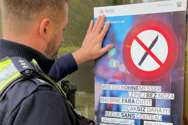 Ein Polizist steht vor einem Hinweisschild für eine Waffenverbotszone wie es sie auch in Dortmund gibt.