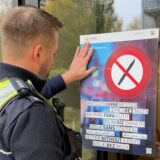 Ein Polizist steht vor einem Hinweisschild für eine Waffenverbotszone wie es sie auch in Dortmund gibt.
