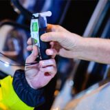 Ein Polizist reicht einem Autofahrer das Alkohol-Atemmessgerät ins Auto.