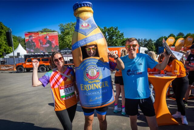 Mehrere Läufer stehen nebeneinander und jubeln. Einer trägt ein überdimensionales Bierflaschen-Kostüm.