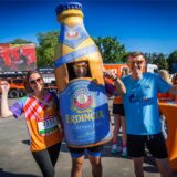 Mehrere Läufer stehen nebeneinander und jubeln. Einer trägt ein überdimensionales Bierflaschen-Kostüm.