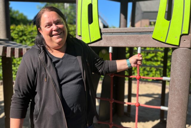 DRK-Juniorkita-Leiterin Iris Gilles steht vor einem Klettergerüst und lacht.