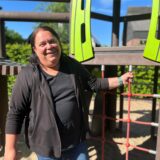 DRK-Juniorkita-Leiterin Iris Gilles steht vor einem Klettergerüst und lacht.
