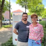 Zwei Personen posieren vor einem Schild mit der Aufschrift „Senioren“. Beide Personen tragen Namensschilder.