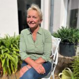 Petra Kussler sitzt in ihrem Hof in der Sonne und lächelt in die Kamera.