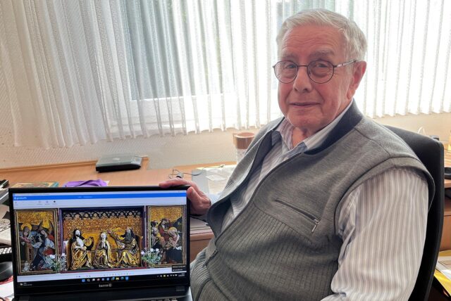 Heinz Wener in seinem Arbeitszimmer mit seinem Laptop, das ein Foto eines Klappaltars zeigt.