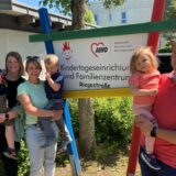 Stehen vor einem Schild der Kita Rappelkiste: (v.l.) Adriane Godiszewski mit Sohn Paul sowie Martina Körner mit Sohn Lio und Robert Körner mit Tochter Ella ein dauerhaftes Ende der Notbetreuung und mehr Verlässlichkeit.