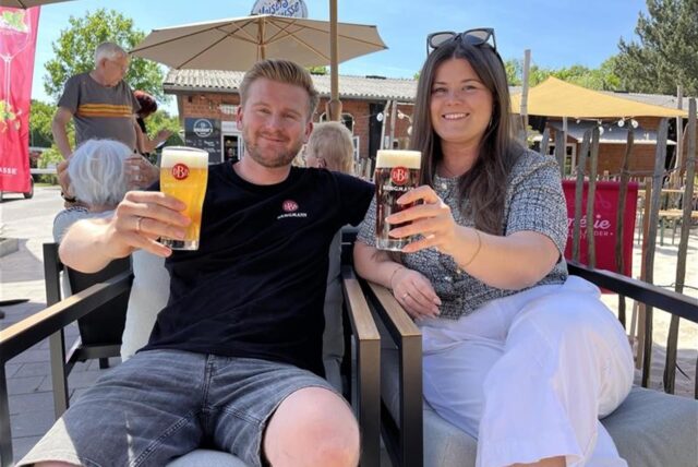 Inhaber Marvin und Anna Bergmann stoßen mit zwei Bergmannbieren in ihrem Biergarten an.