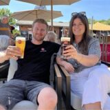 Inhaber Marvin und Anna Bergmann stoßen mit zwei Bergmannbieren in ihrem Biergarten an.
