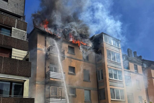 Schwarzer Rauch quillt aus dem Dach eines braunen Altbaugebäudes.