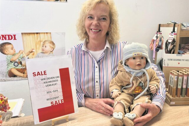 Christiane Karls mit Puppe kündigt den Räumungsverkauf an.